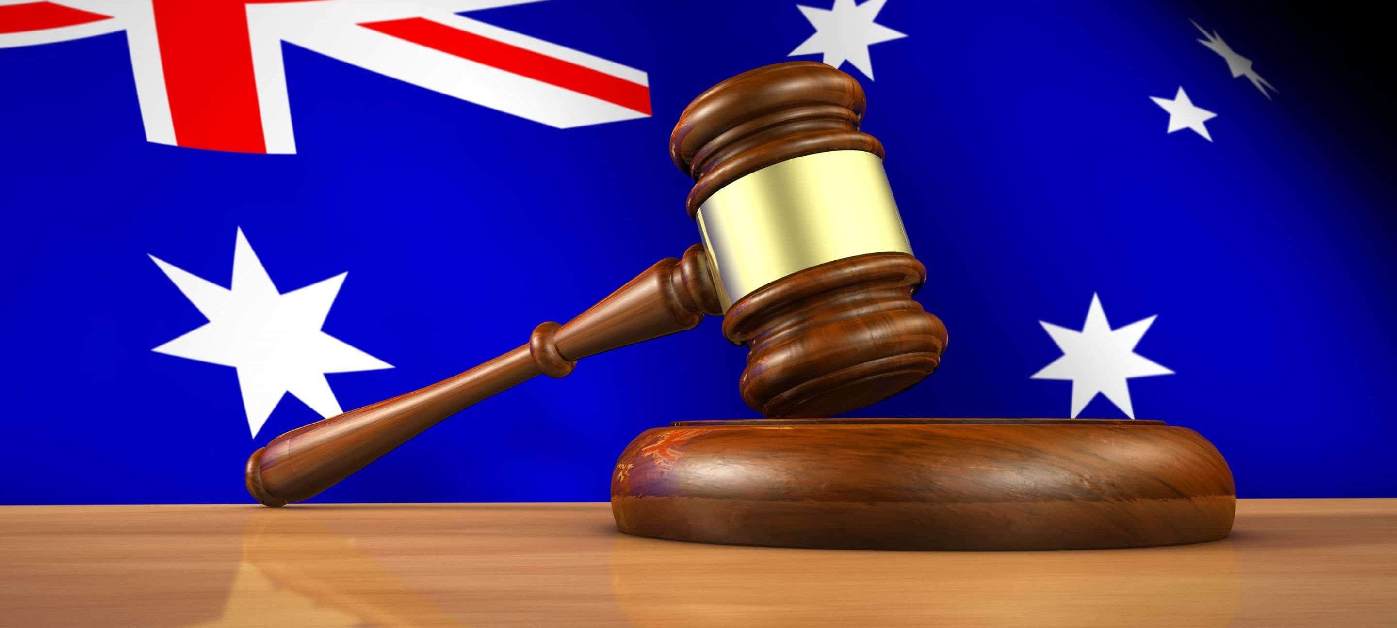 A wooden gavel resting on its round sound block on a pale timber bench, in front of a large Australian flag.